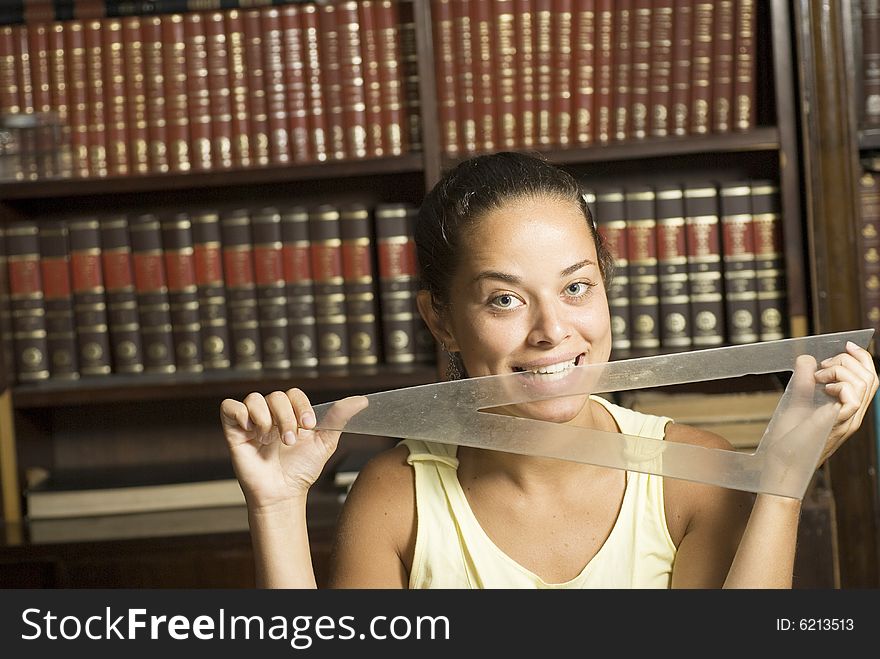 Woman playfully biting on a protractor with books in the background. Horizontally framed photo. Woman playfully biting on a protractor with books in the background. Horizontally framed photo