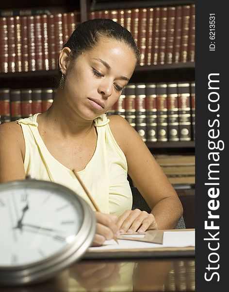 Student working while seated at a desk in an office surrounded by books and a clock. Vertically framed photo. Student working while seated at a desk in an office surrounded by books and a clock. Vertically framed photo.