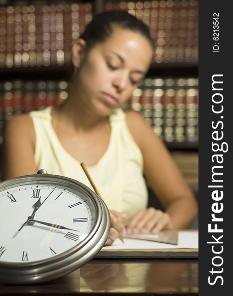 Girl in office with books writing at desk beside a clock. Horizontally framed photo. Girl in office with books writing at desk beside a clock. Horizontally framed photo.