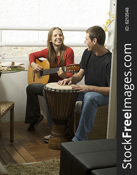 Woman playing guitar as she smiles at the man next to her on the drums. Vertically framed photo. Woman playing guitar as she smiles at the man next to her on the drums. Vertically framed photo.