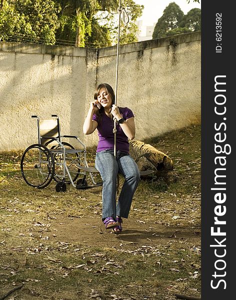 Girl in rope swing talking on phone with wheelchair nearby. Vertically framed photo. Girl in rope swing talking on phone with wheelchair nearby. Vertically framed photo.