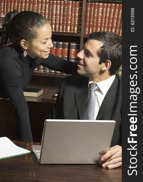 Businessman and woman smiling at each other surrounded by books and a laptop. Vertically framed photo. Businessman and woman smiling at each other surrounded by books and a laptop. Vertically framed photo.