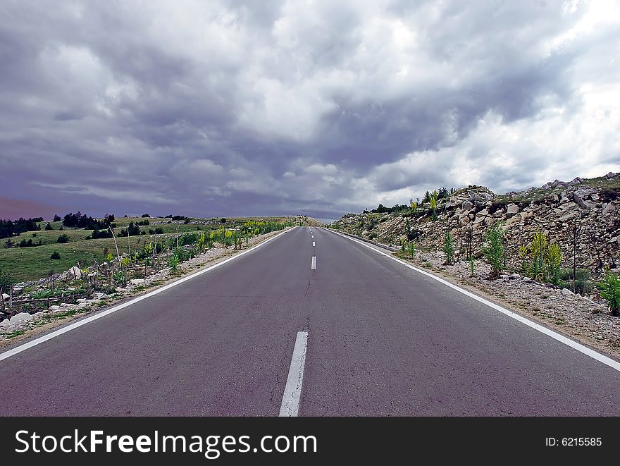 Gray road through mountain landscape under cloudy sky. Gray road through mountain landscape under cloudy sky