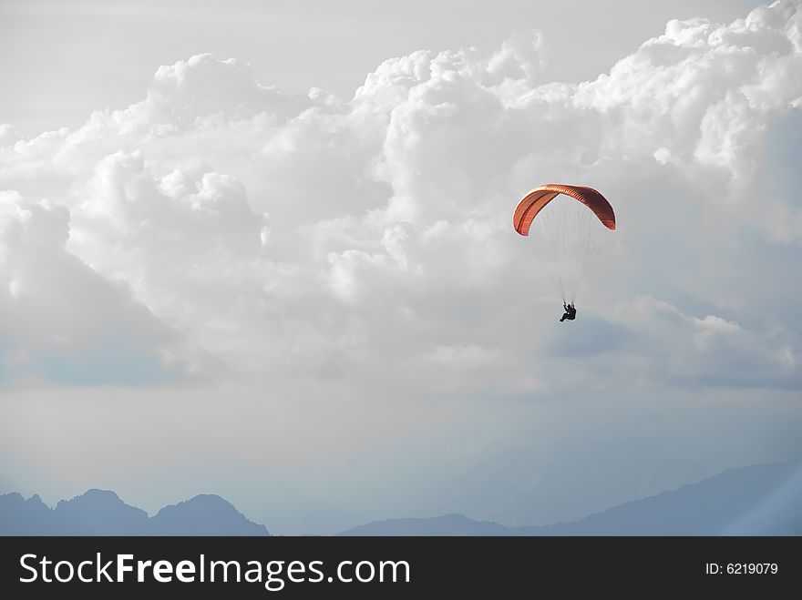 A paraglider beneath a beautiful sky and above some mountains. A paraglider beneath a beautiful sky and above some mountains