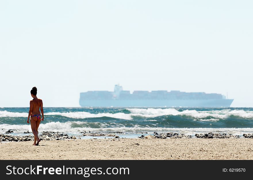 Woman going along the beach against big ship on the horizon of the sea. Woman going along the beach against big ship on the horizon of the sea