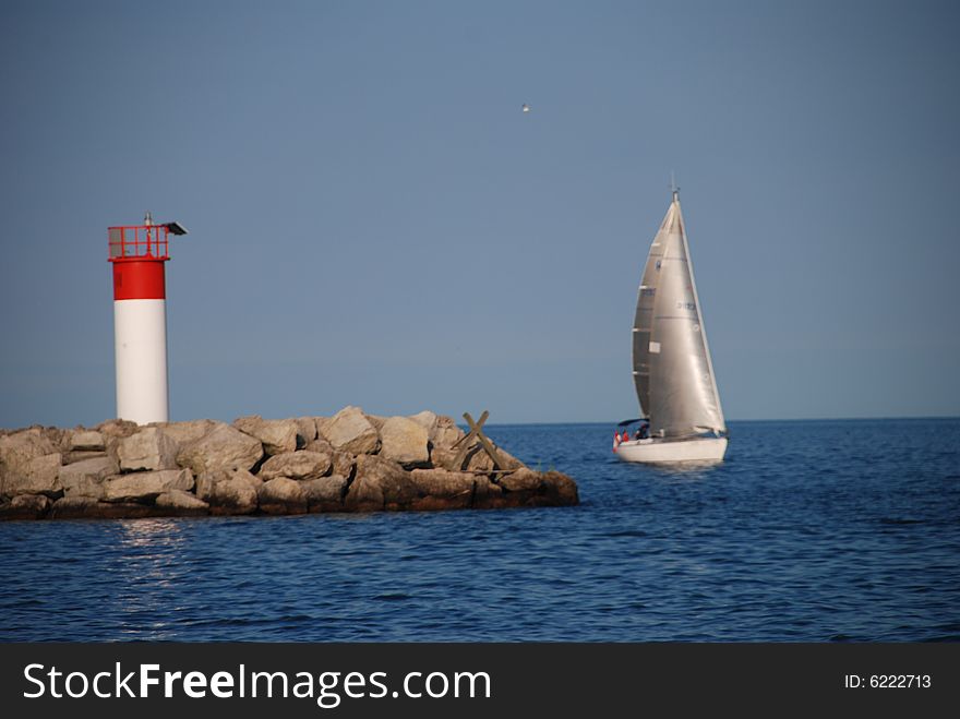 A silver sailboat and a red lighthouse near a harbour. A silver sailboat and a red lighthouse near a harbour