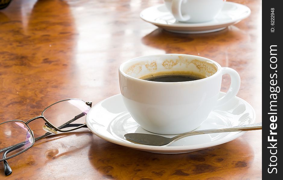 Two cups of partly drank coffee, and a pair of spectacles, on a marbled table top in the afternoon. Two cups of partly drank coffee, and a pair of spectacles, on a marbled table top in the afternoon