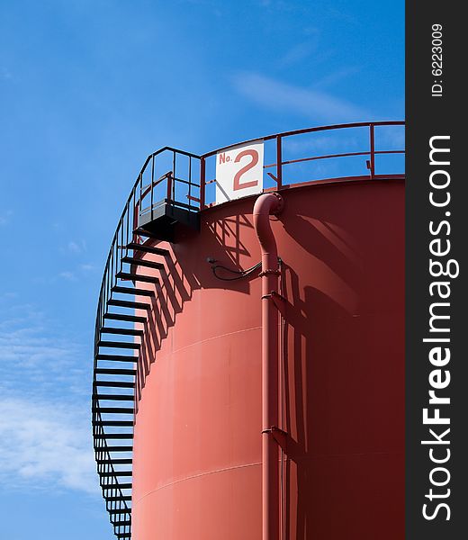 Red colored tank with a spiral staircase to its roof in a blue sky. Red colored tank with a spiral staircase to its roof in a blue sky