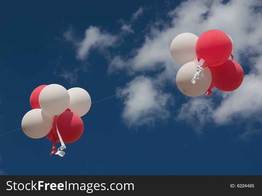 Red and white balloons with ribbons against blue sky.