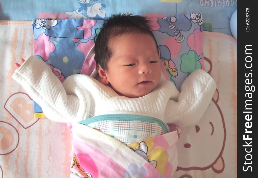 A Chinese baby is waving her hand on a bed. A Chinese baby is waving her hand on a bed