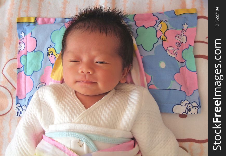 A Chinese infant is smiling on a bed. A Chinese infant is smiling on a bed