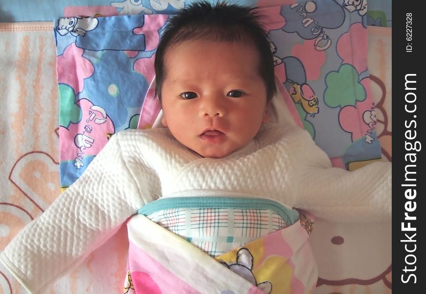 A Chinese infant is waving her hand on the bed. A Chinese infant is waving her hand on the bed