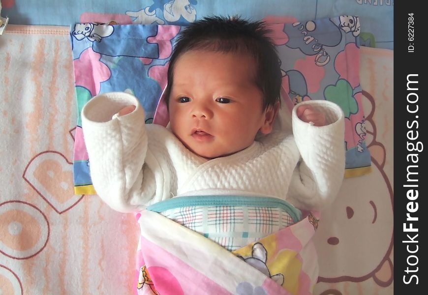 A Chinese infant is waving her hand on the bed. A Chinese infant is waving her hand on the bed