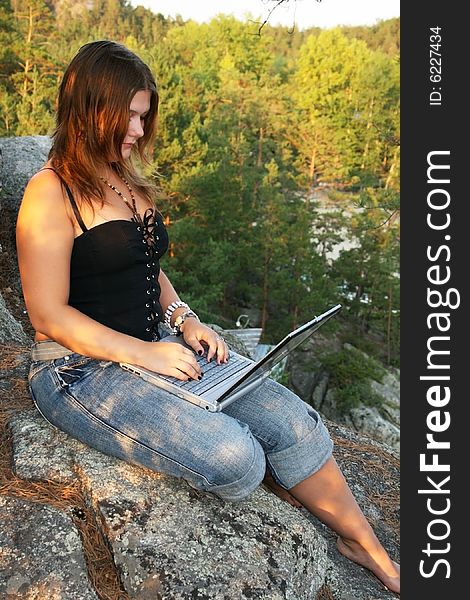 Female hiker taking a break at the edge of a cliff to check her email on her laptop. Female hiker taking a break at the edge of a cliff to check her email on her laptop.