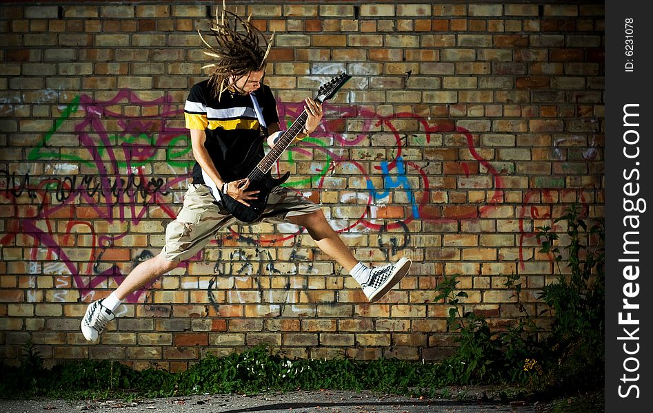 Young man with guitar jumping against the wall. Young man with guitar jumping against the wall.