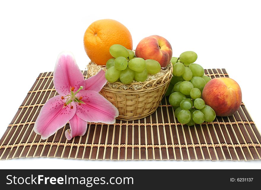 Beautiful flower of a lily and fruit in a yellow basket on a striped brown napkin on a white background