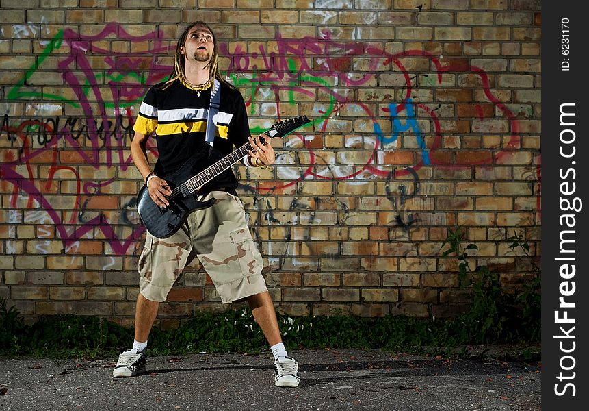 Young man standing with guitar against the wall. Young man standing with guitar against the wall.