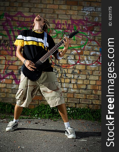 Young man playing the guitar and singing against the wall. Young man playing the guitar and singing against the wall.