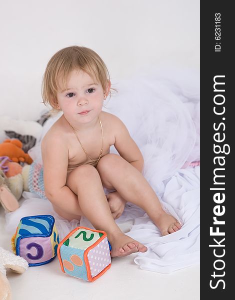 Little naked girl is seating with her toys