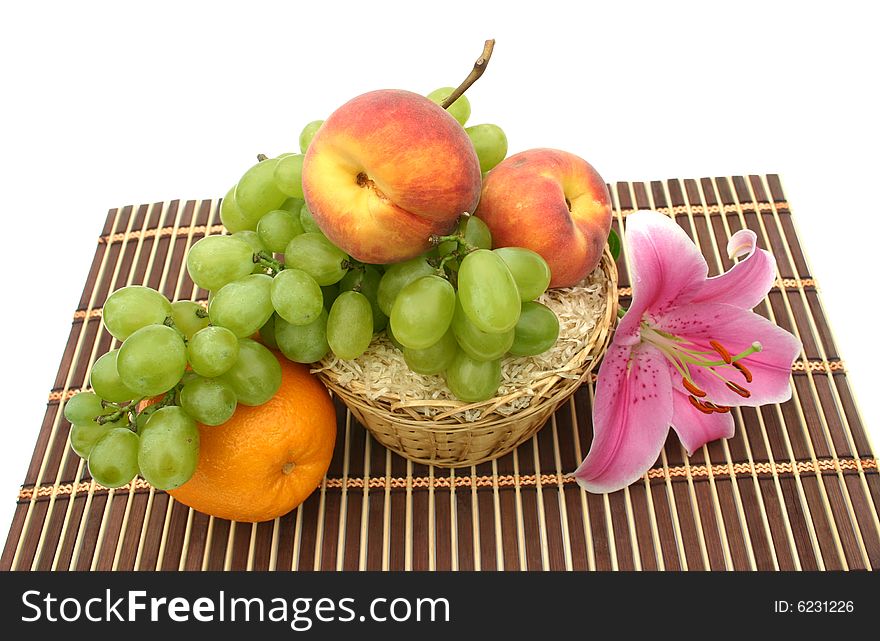 Beautiful flower of a lily and fruit in a yellow basket on a striped brown napkin on a white background. Beautiful flower of a lily and fruit in a yellow basket on a striped brown napkin on a white background