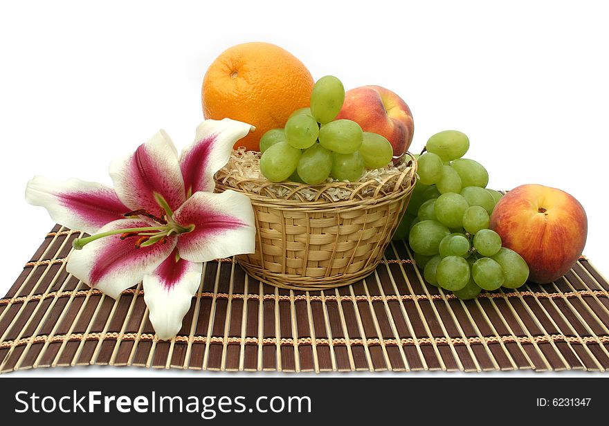 Beautiful flower of a lily and fruit in a yellow basket on a striped brown napkin on a white background