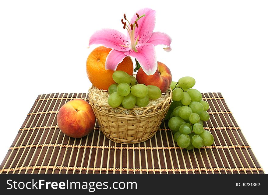 Beautiful flower of a lily and fruit in a yellow basket on a striped brown napkin on a white background