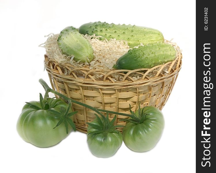 Cluster of green tomatoes and green cucumbers in a basket on a white background