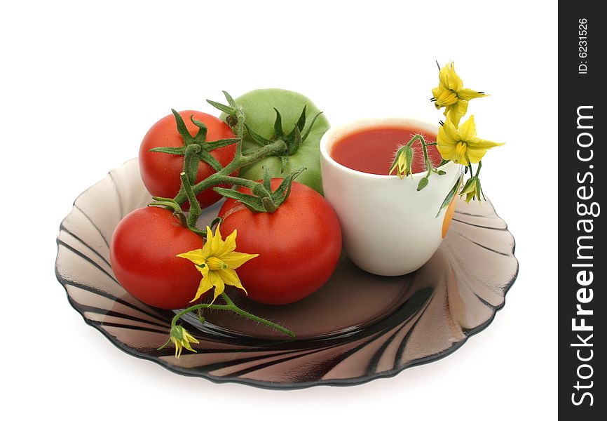 Red tomatoes on a black plate with a white cup of tomato juice on a white background. Red tomatoes on a black plate with a white cup of tomato juice on a white background