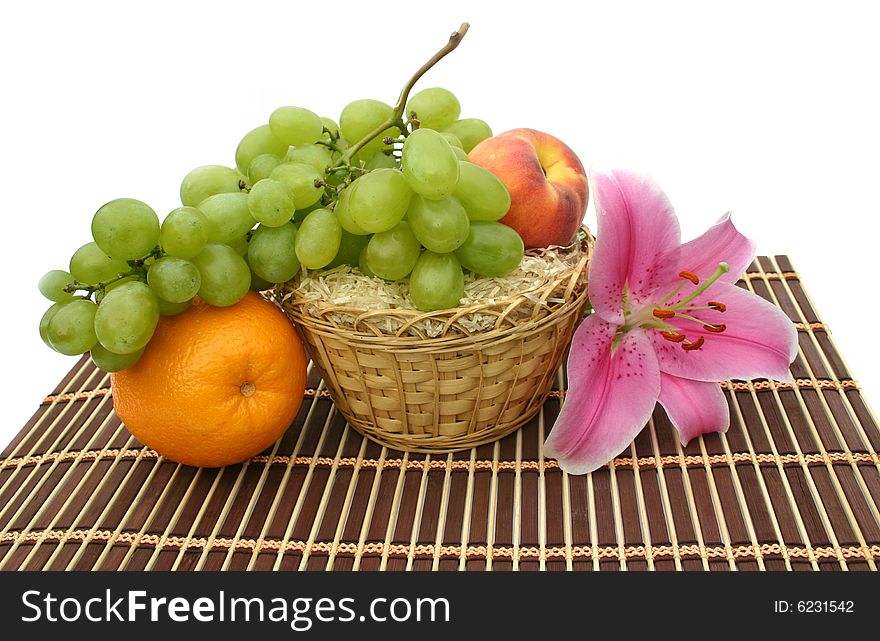 Flower of a lily and fruit in a yellow basket on a striped brown napkin on a white background