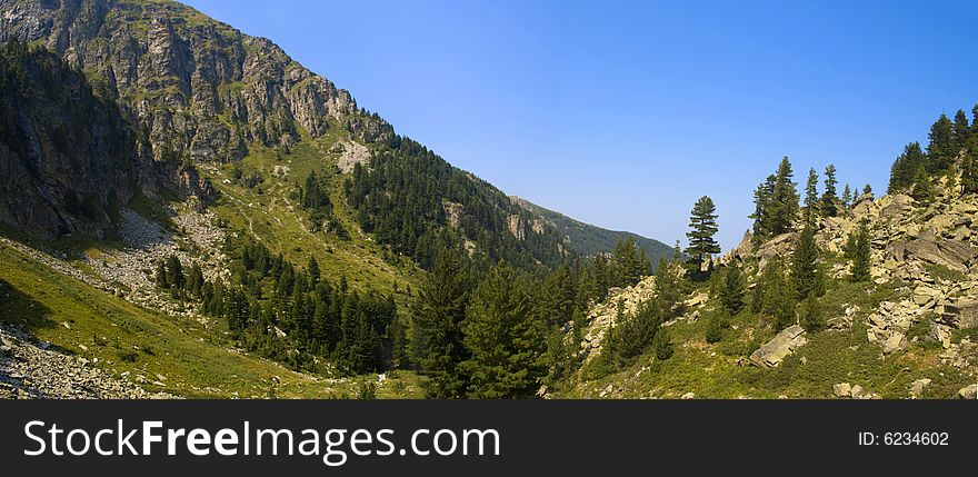 A panorama of beautiful mountain valley full of trees and rocks on a sunny summer day. A panorama of beautiful mountain valley full of trees and rocks on a sunny summer day