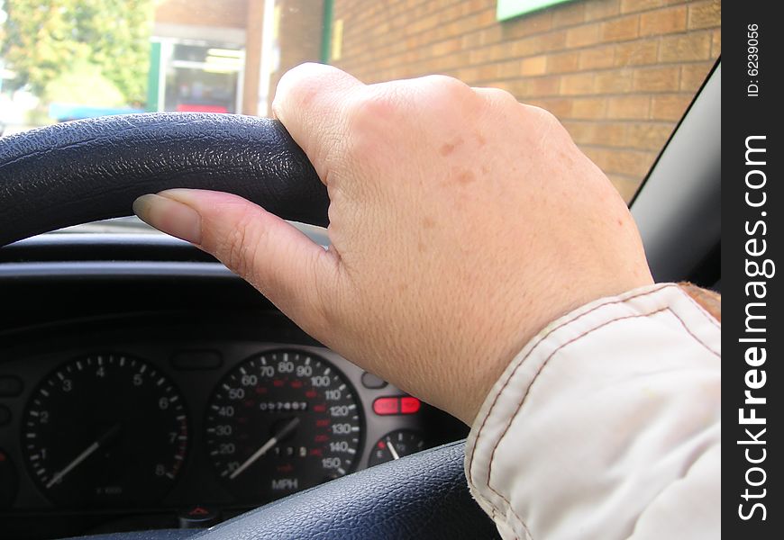 Hand on a steering wheel of a car as the person drives along the road. Hand on a steering wheel of a car as the person drives along the road