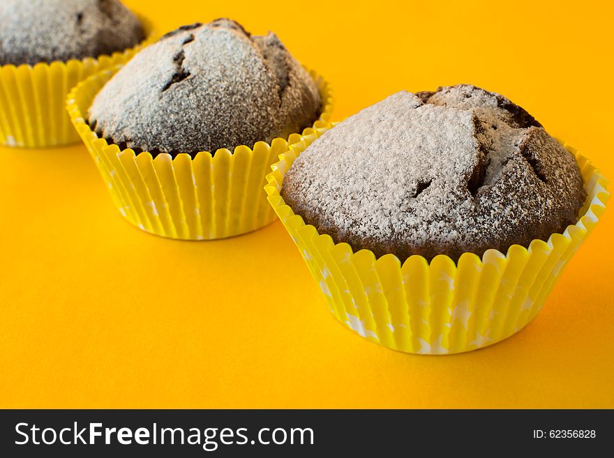 Chocolate muffins in paper cupcake holder on yellow background, selective focus. Chocolate muffins in paper cupcake holder on yellow background, selective focus