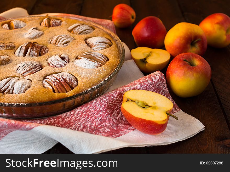 Apple pie in a baking dish, linen napkin and apples on dark background, selective focus. Apple pie in a baking dish, linen napkin and apples on dark background, selective focus