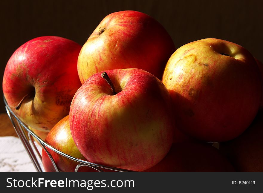 Red apples in a metal basket lit by the sun from a window