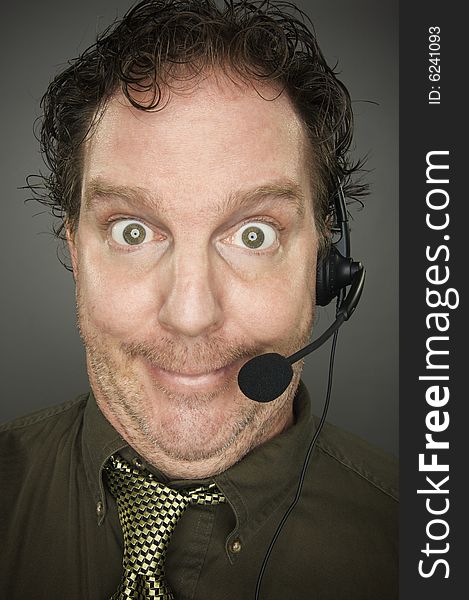 Giddy Businessman Smiles Wearing a Phone Headset Against a Grey Background.