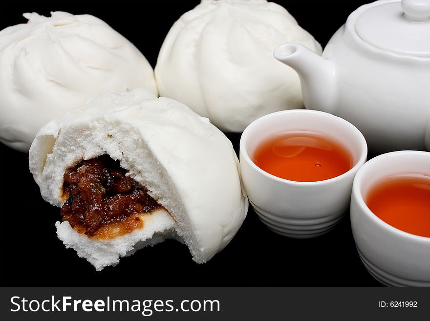 Chinese barbecued pork bun with teapot and teacups on black background.