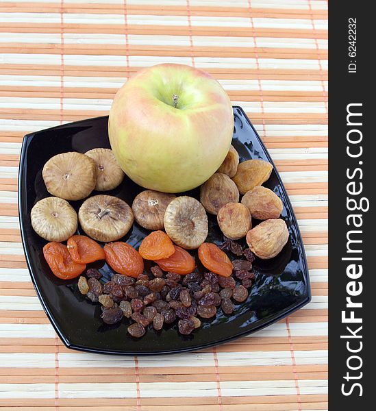 Dry fruit and apple on a black plate