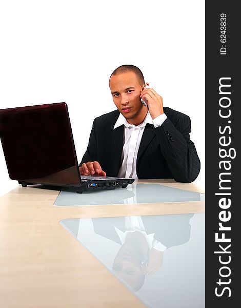 A young businessman sitting by desk at office working on the laptop while talking on cellphone. Isolated over white. A young businessman sitting by desk at office working on the laptop while talking on cellphone. Isolated over white.