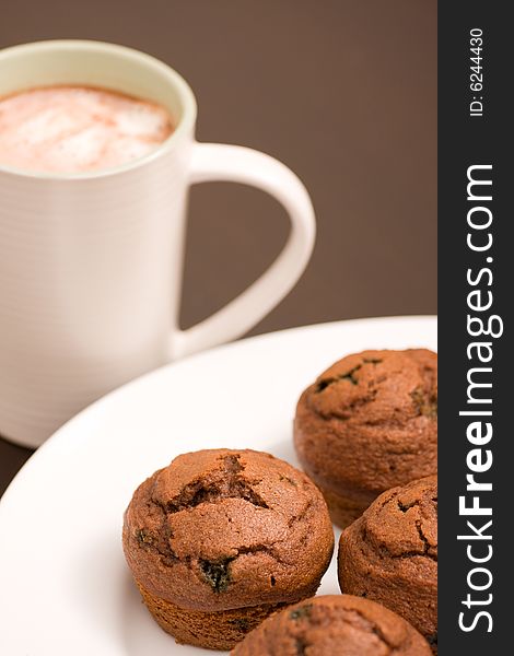 Freshly baked muffins on a white serving plate and hot chocolate in a white cup. Freshly baked muffins on a white serving plate and hot chocolate in a white cup