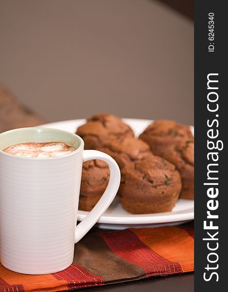 A cup of foaming hot chocolate and chocolate mint muffins. A cup of foaming hot chocolate and chocolate mint muffins