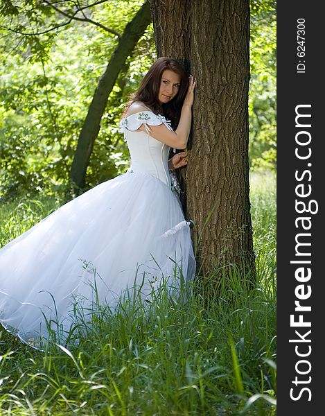 The bride stands near a tree and looks in the cam. The bride stands near a tree and looks in the cam