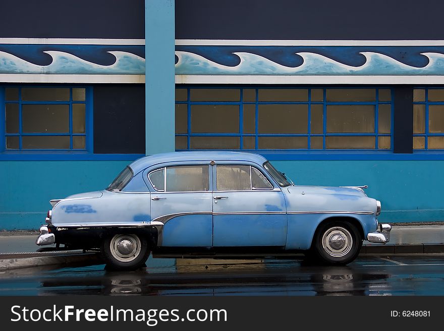 It is an old blue car in front of a similar colourd wall with waves.