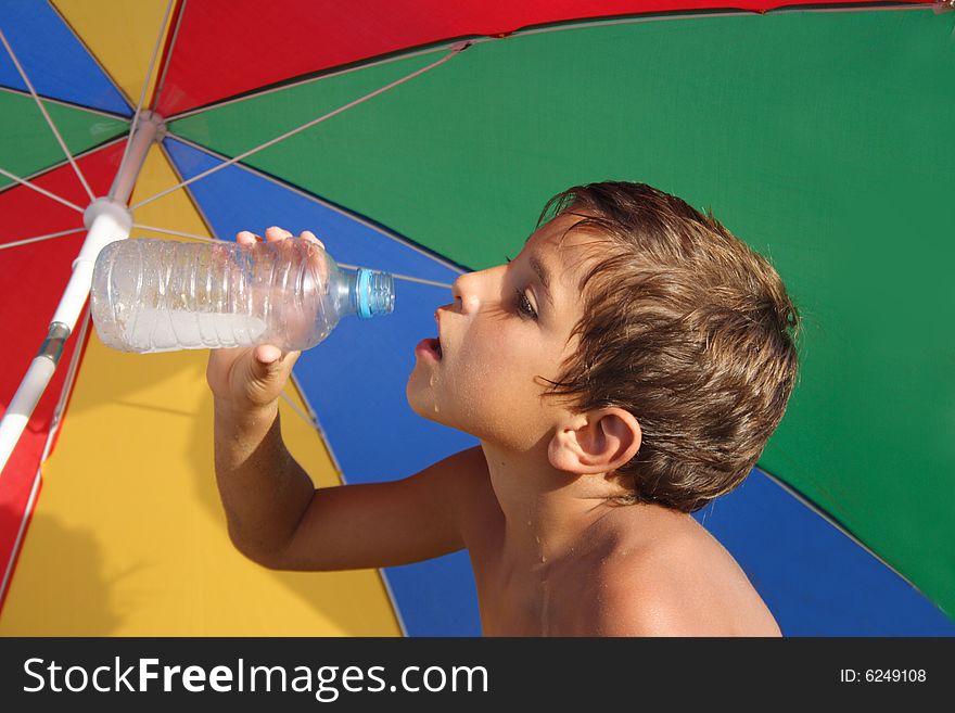 Boy drinking water under the colorful parasol. Boy drinking water under the colorful parasol