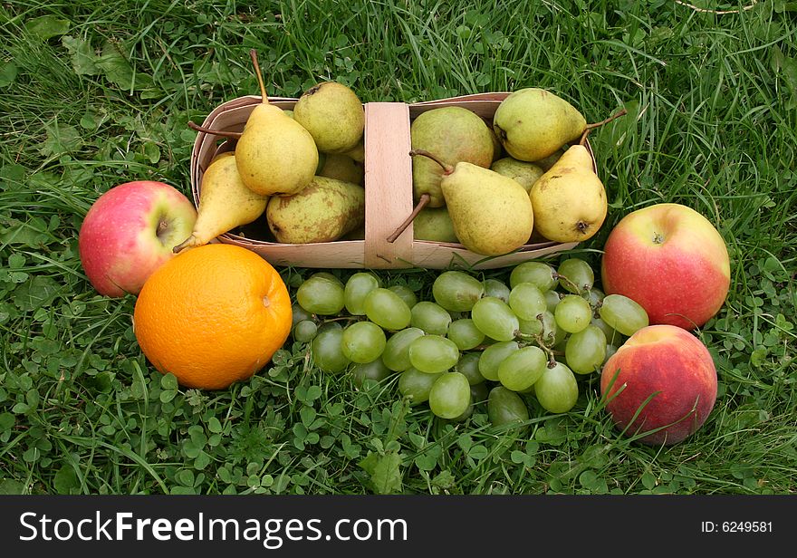 Pears and apples with a peach on a green grass in a basket