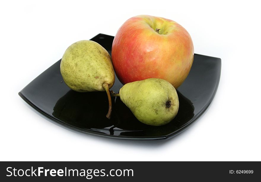 Yellow pears and a ripe apple on a black plate 
on a white background. Yellow pears and a ripe apple on a black plate 
on a white background