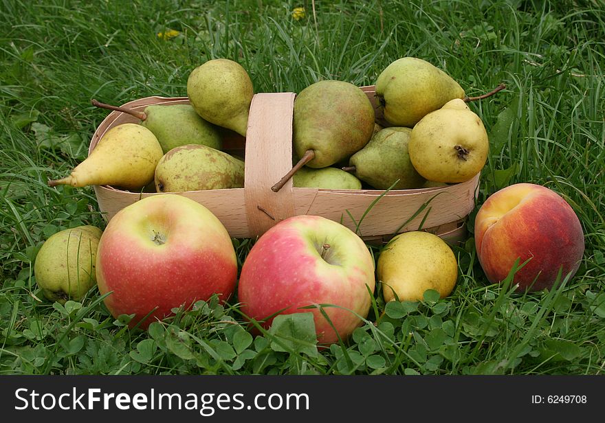 Pears and apples with a 
peach on a green grass in a basket