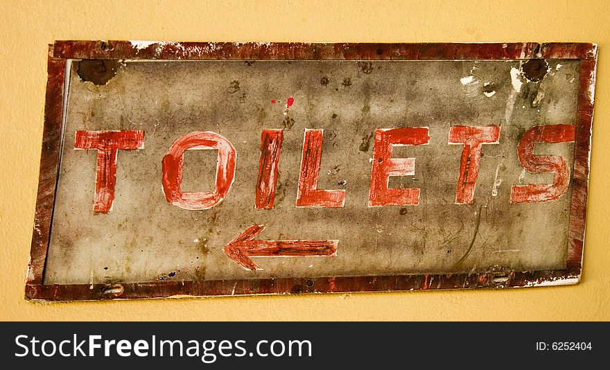 Old rustic sign showing way to toilets on yellow wall with red lettering. Old rustic sign showing way to toilets on yellow wall with red lettering