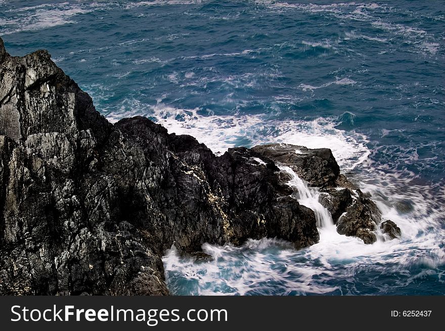 Large rockface in the ocean. Water is intentionally blurred.