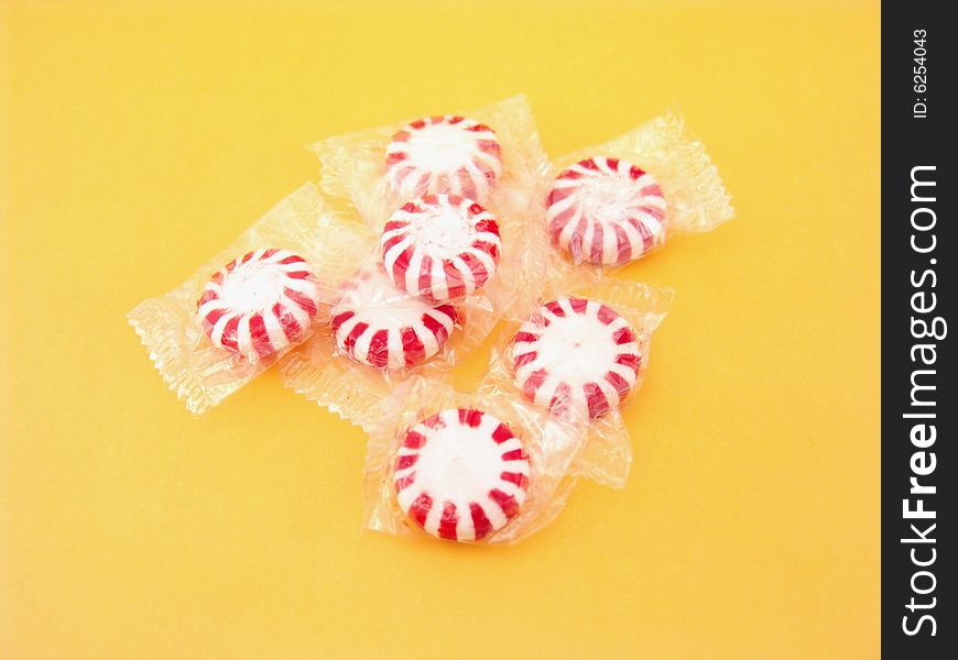 Red and white peppermints in plastic wrappers over yellow background