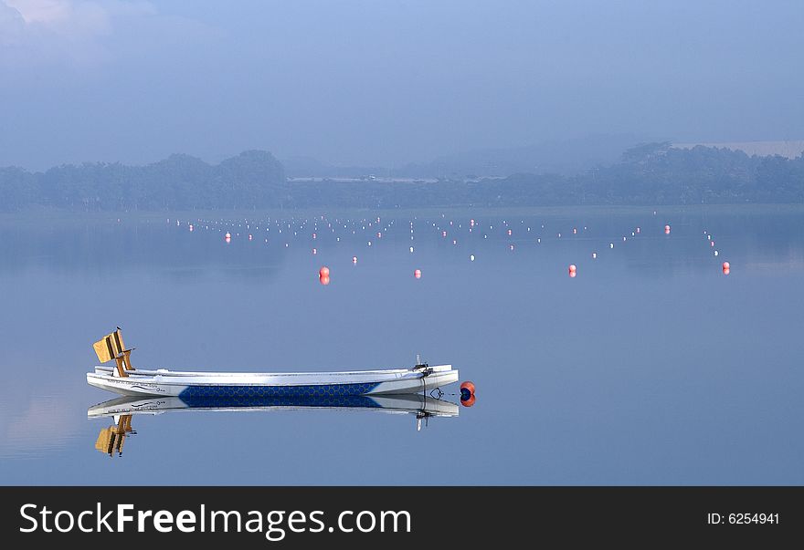 A sporting boat in a lake/reservior in Singapore in a foggy morning with red ball marked racing lane as background. A sporting boat in a lake/reservior in Singapore in a foggy morning with red ball marked racing lane as background.